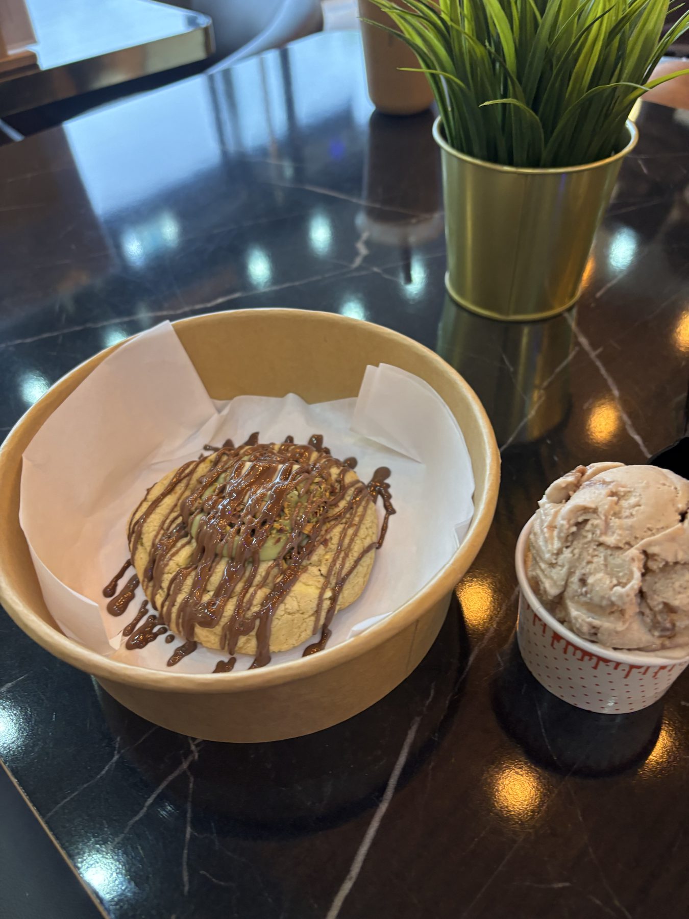 A pistachio cookie in a paper bowl beside a scoop of gelato.